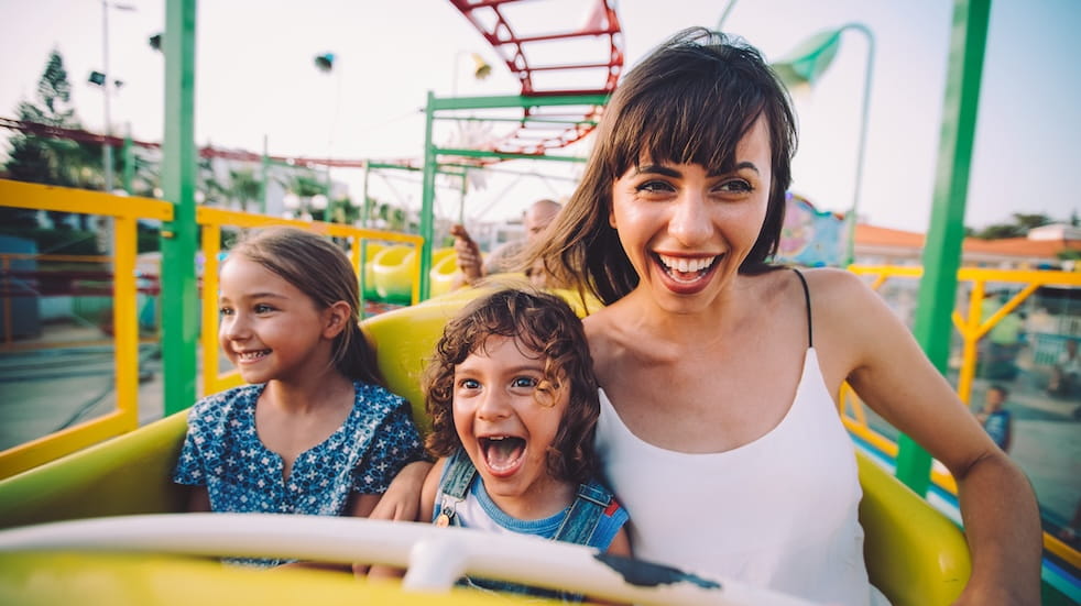 Excited little boy and girl having fun with mother riding amusement park roller coaster
